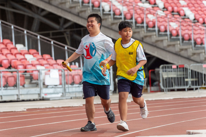 Athlete and unified partner participating in relay run sport competition on a track field.